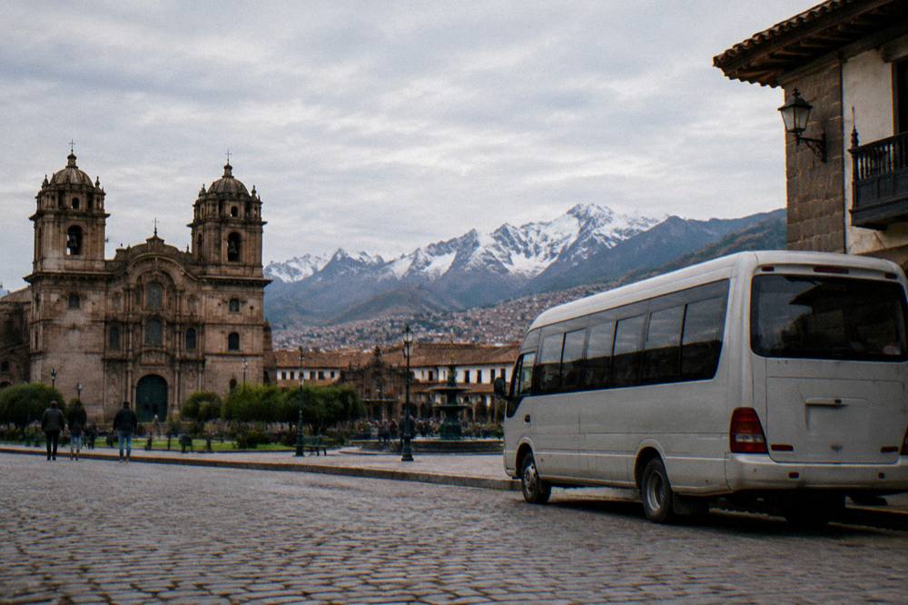 A parked tour minibus on a high Andean road with snow-covered peaks in the distance