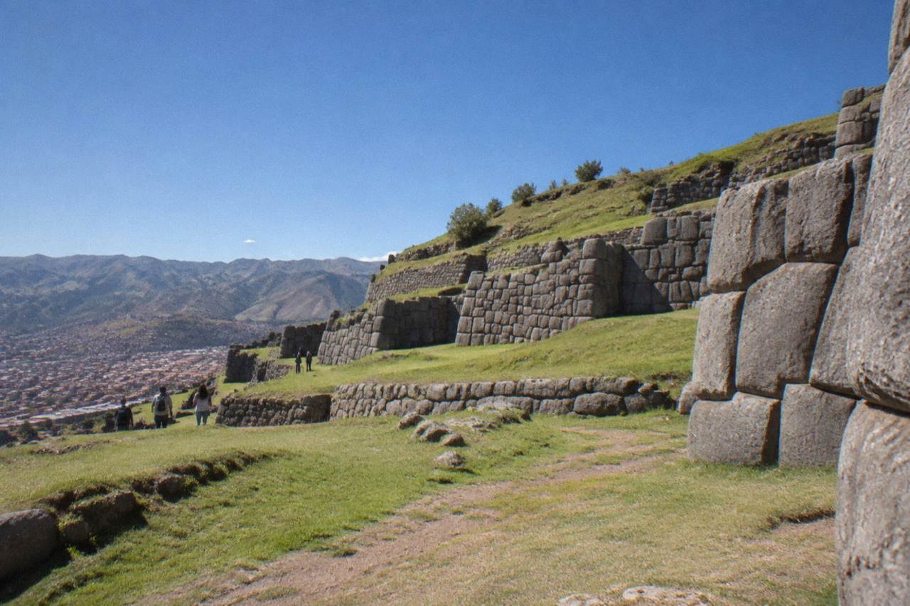 Terraced Inca stone walls on a green hillside above the city of Cusco under a clear sky