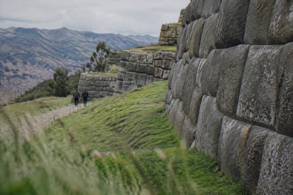 Large fitted limestone blocks of an Inca wall in Cusco with a sloping grass terrace beside them