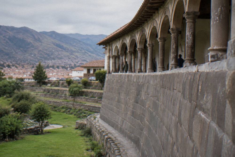 Curved finely cut stone wall of Qorikancha with a colonial arched walkway above it