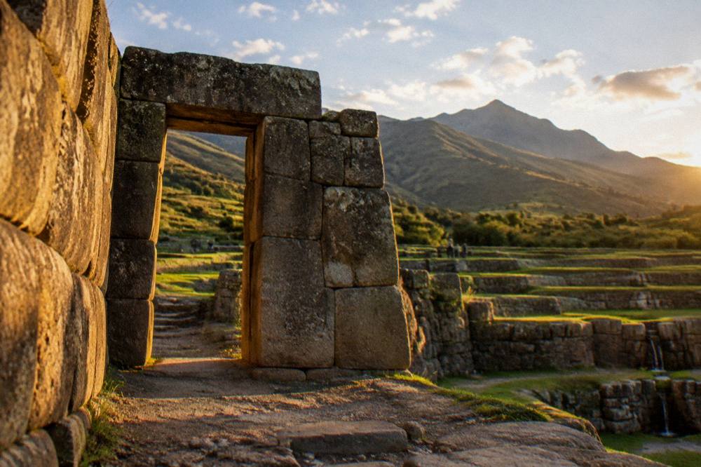 Stone gateways and agricultural terraces of an Inca site with green fields and mountains beyond