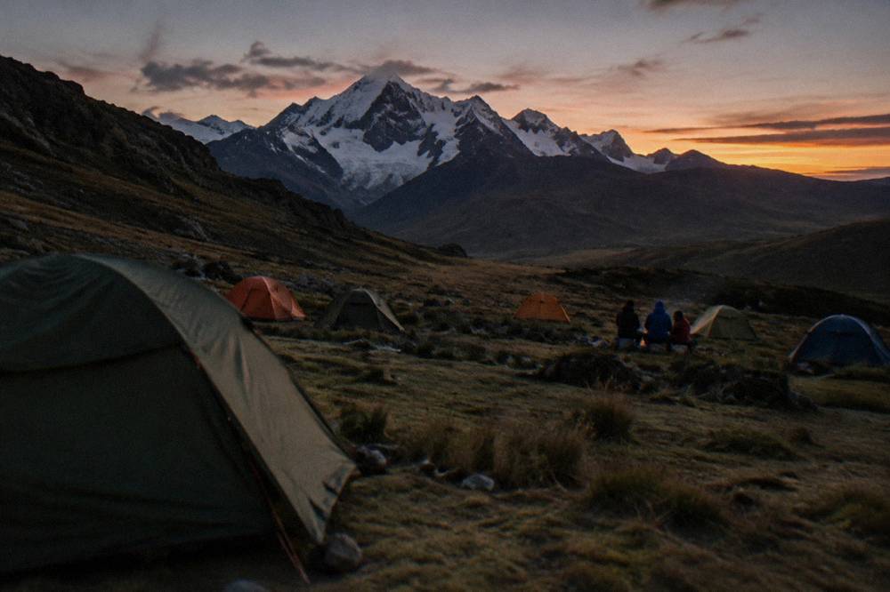 A trekking camp of small tents pitched on a grassy Andean plateau at dusk