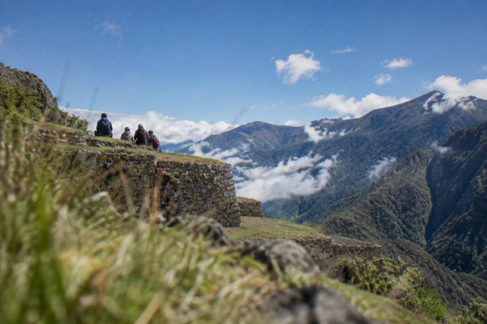 Trekkers with backpacks resting on a stone terrace above a valley of cloud forest