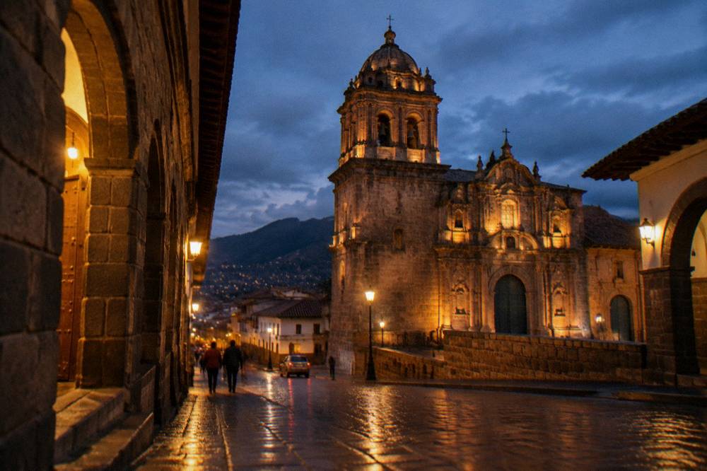 An evening street in Cusco with warm light from doorways, stone archways and wet paving reflecting the lamps