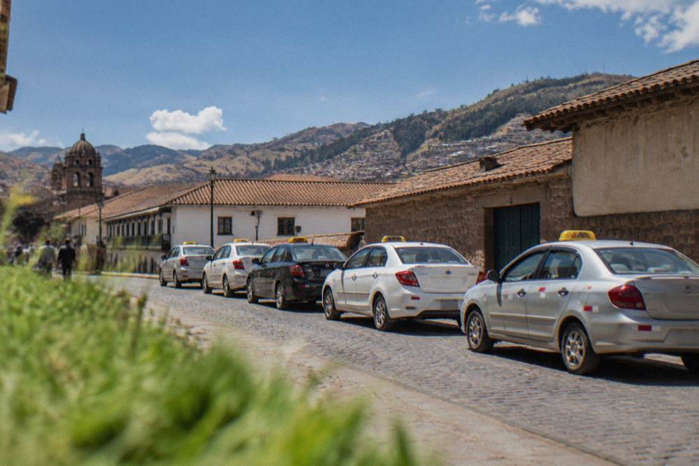 A row of taxis parked in a line on a city street in the early morning with hills behind the rooftops