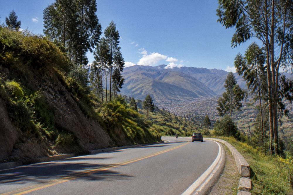 A paved Andean road curving through a green valley with eucalyptus trees and distant mountains