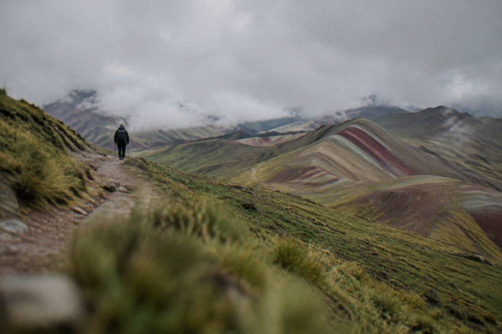 A hiker on a high Andean trail with striped hills in the distance