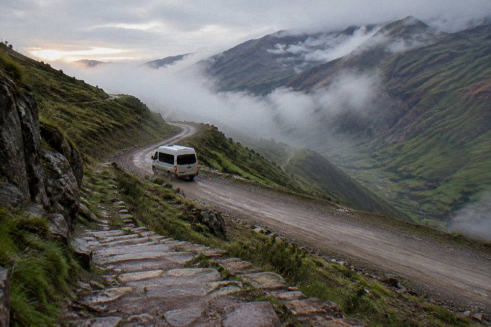A minibus on a winding unpaved mountain road at dawn