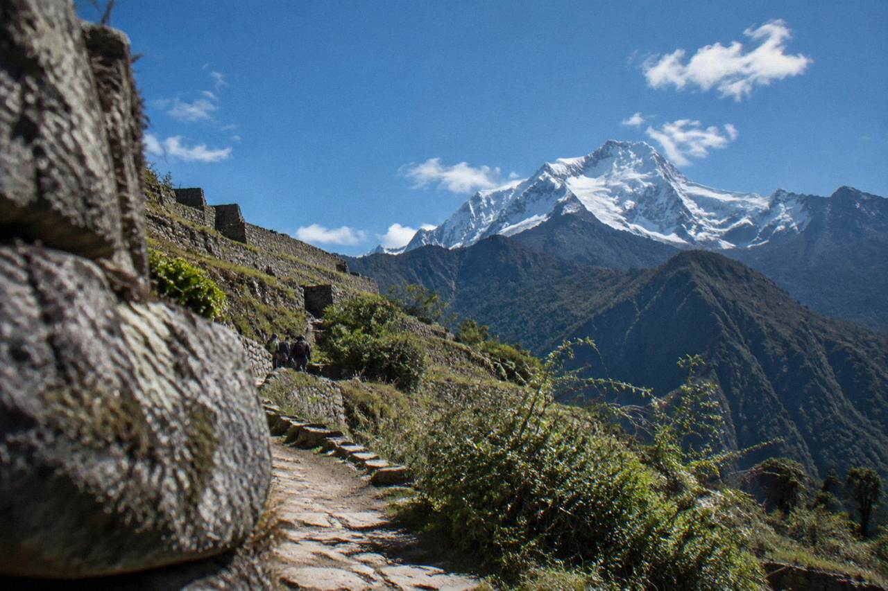 A snow-covered Andean peak rising above a high mountain trail under a clear blue sky