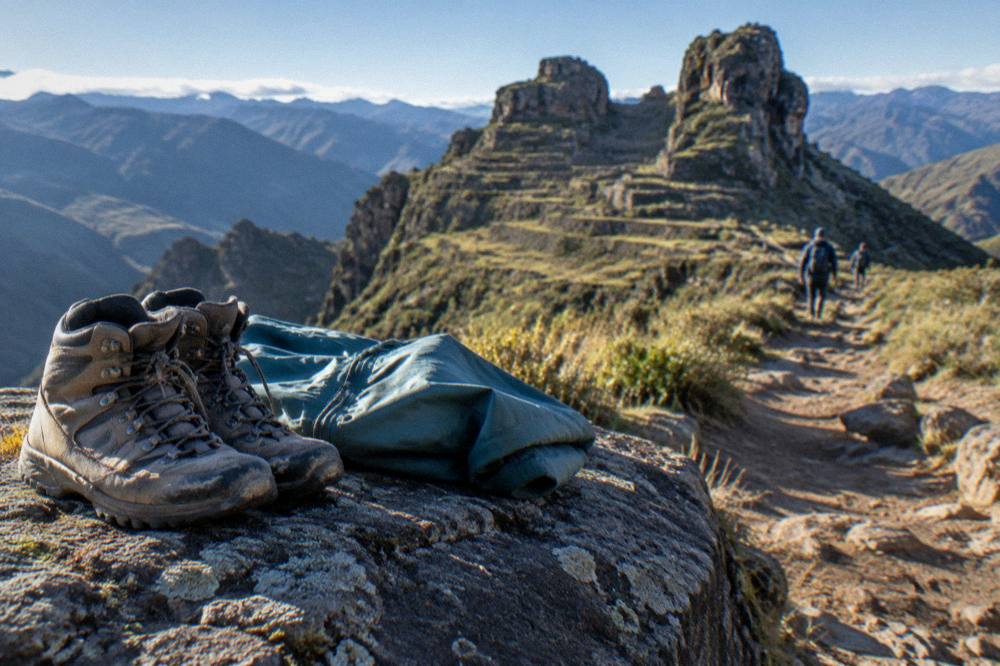 A pair of worn hiking boots and a folded rain jacket on a rock beside a mountain trail