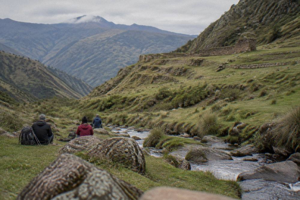A small group of trekkers resting beside a stream in a green high Andean valley