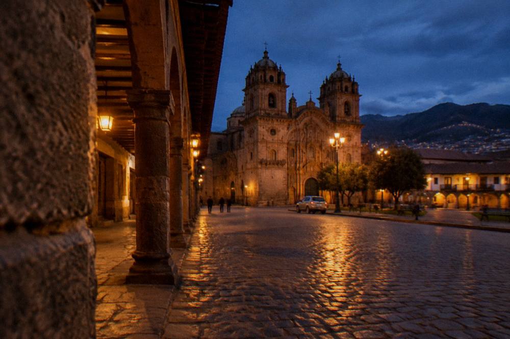 A quiet colonial plaza at dusk with stone arcades and warm street lighting