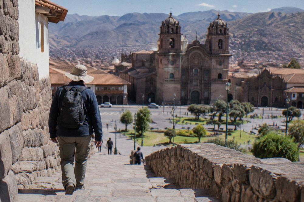 Traveller in a fleece jacket and sun hat walking a stone stairway in bright Andean sunlight