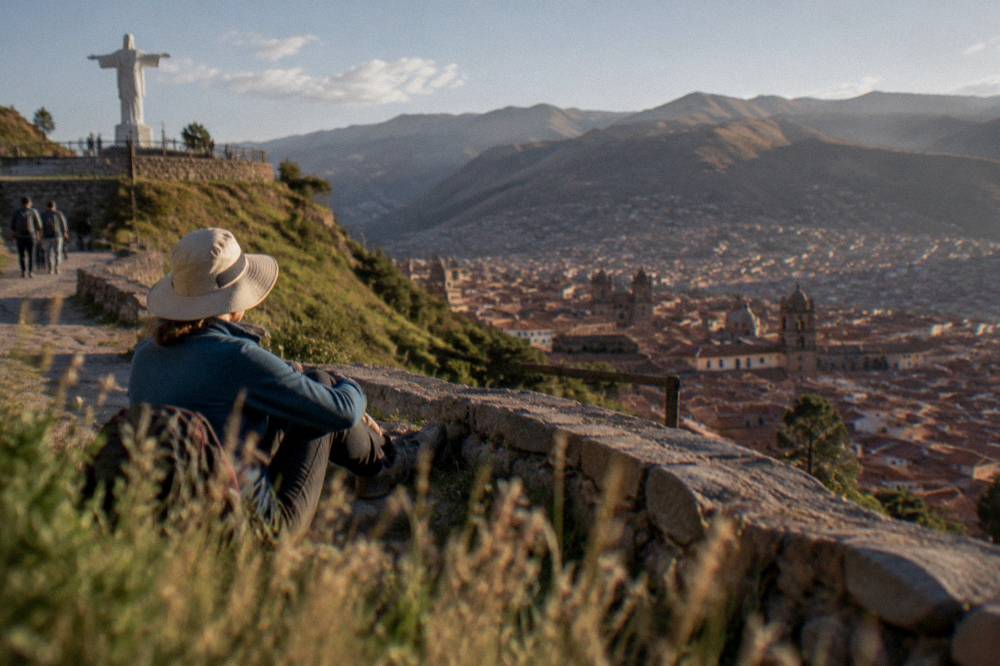 Layered traveller in fleece and sun hat resting on a sunny terrace above Cusco rooftops