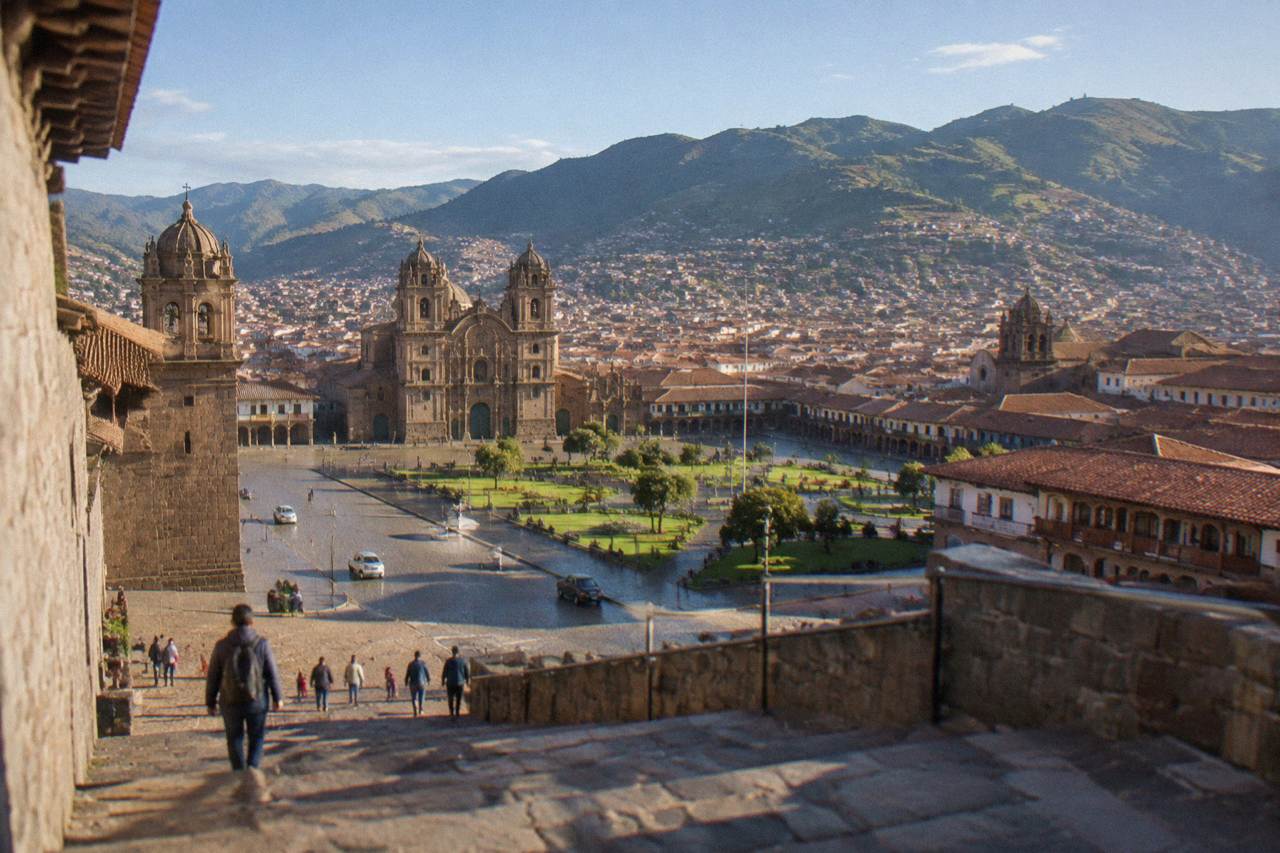 Terracotta rooftops of a high Andean city spreading across a valley below green hills