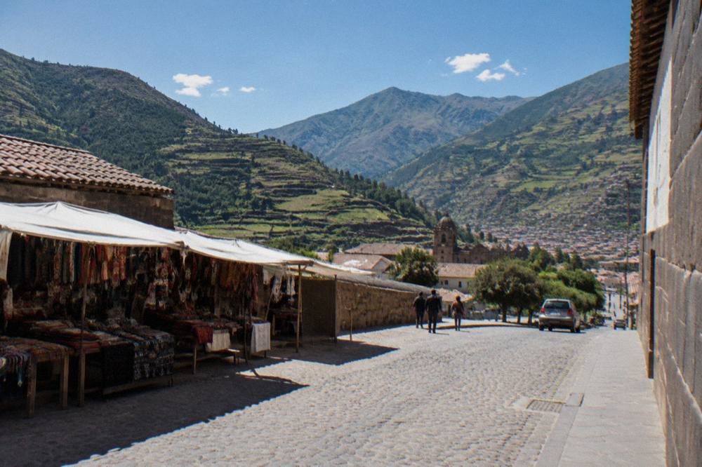 A high Andean valley with agricultural terraces cut into green slopes under a blue sky