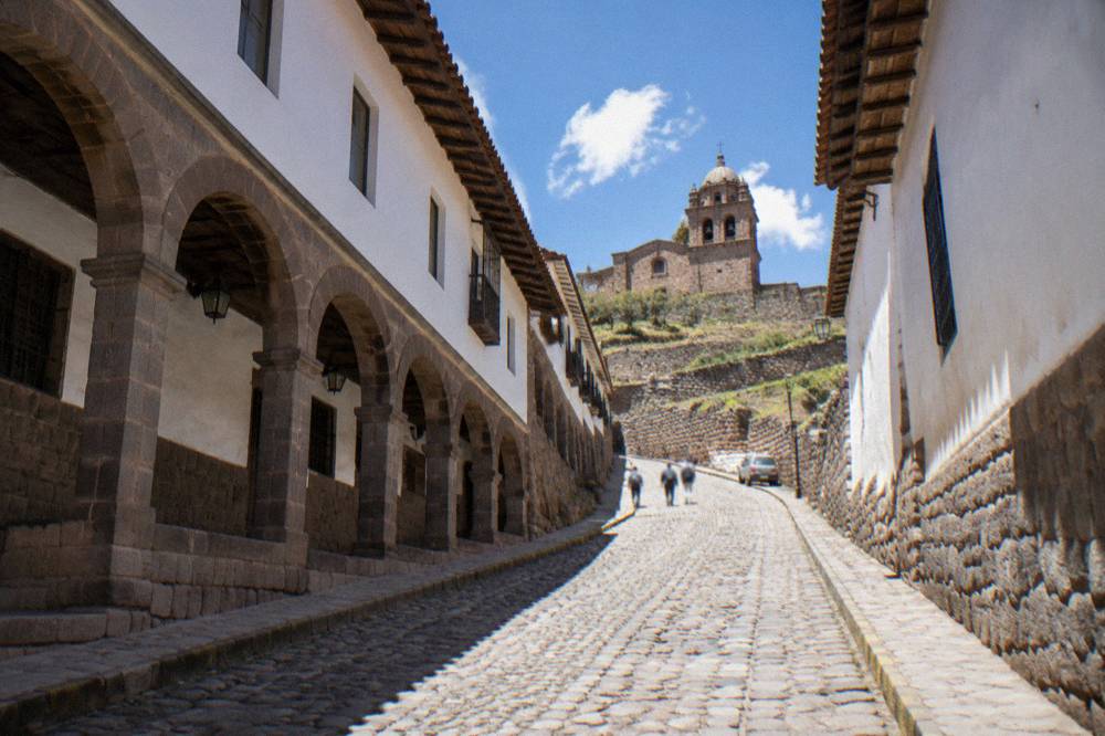 A steep cobblestone street with colonial arcades climbing toward a hillside church