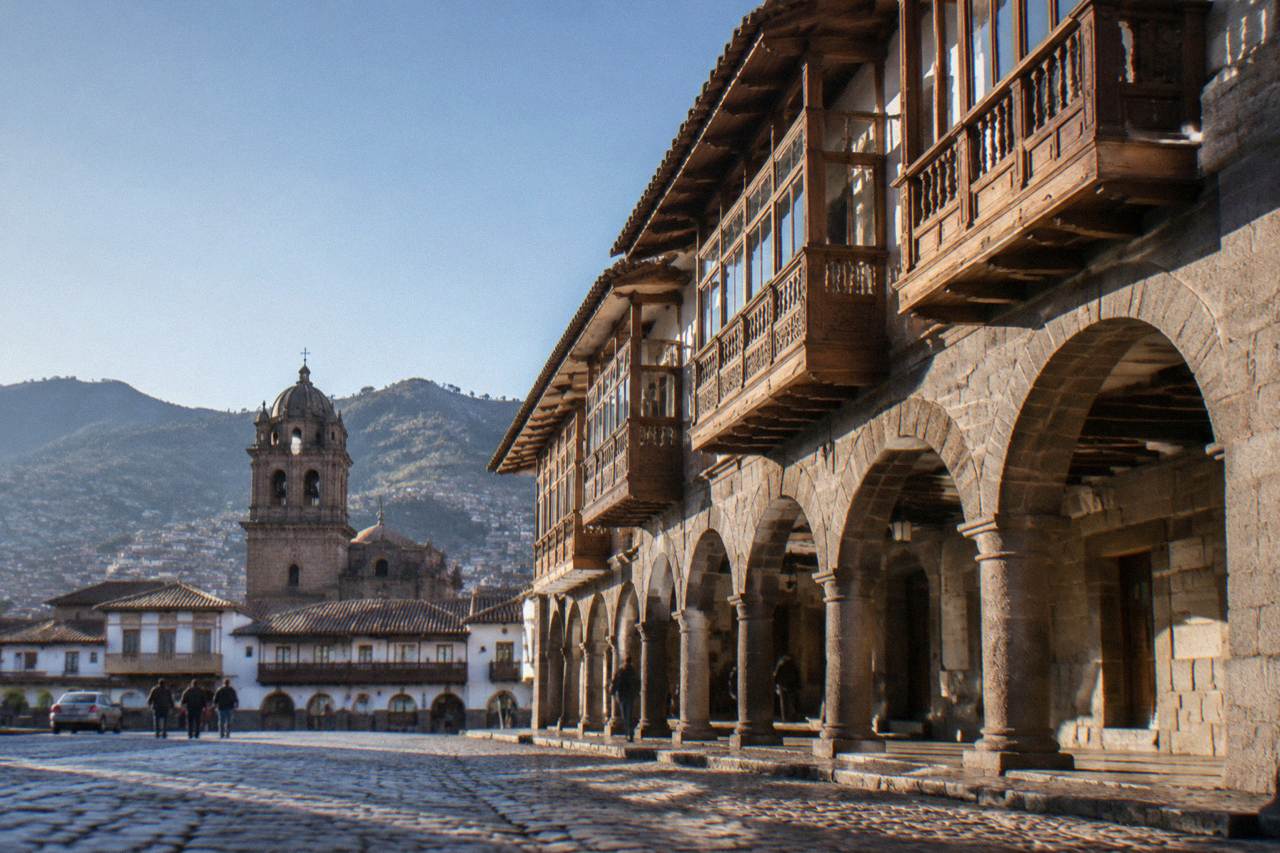 Stone arcades and church towers around a plaza in an Andean city at dusk