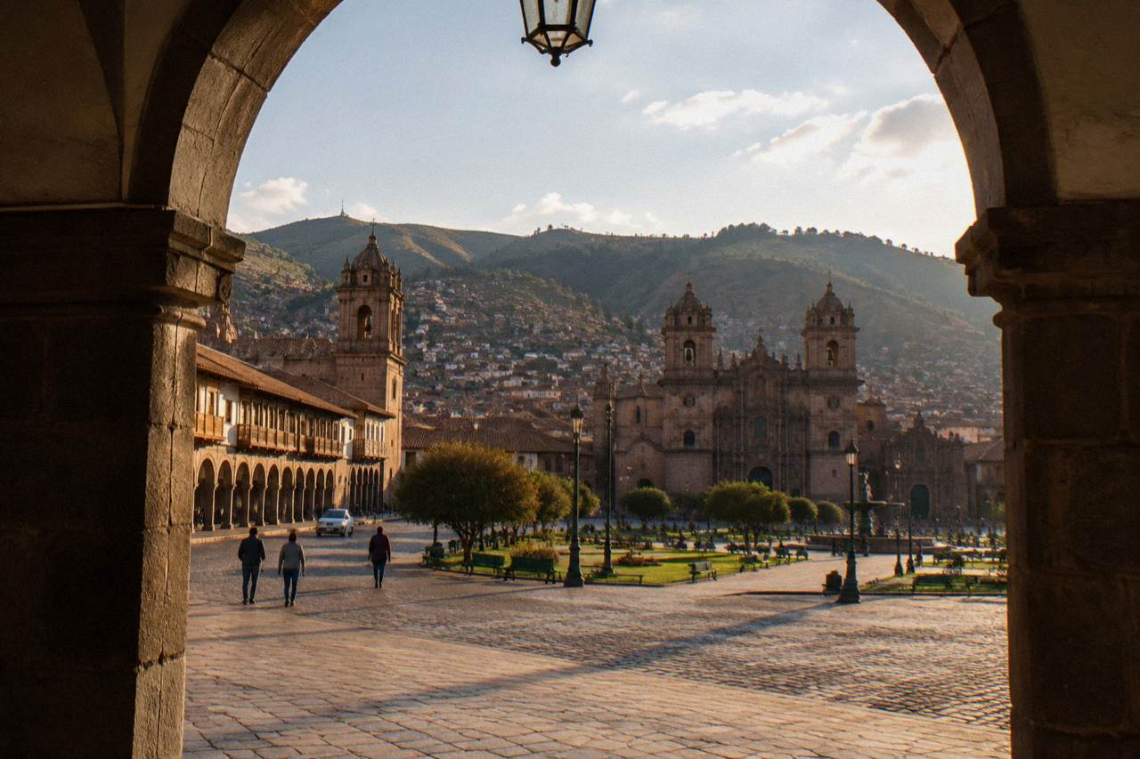 Colonial arcades and stone churches around a wide plaza in Cusco with green hills behind