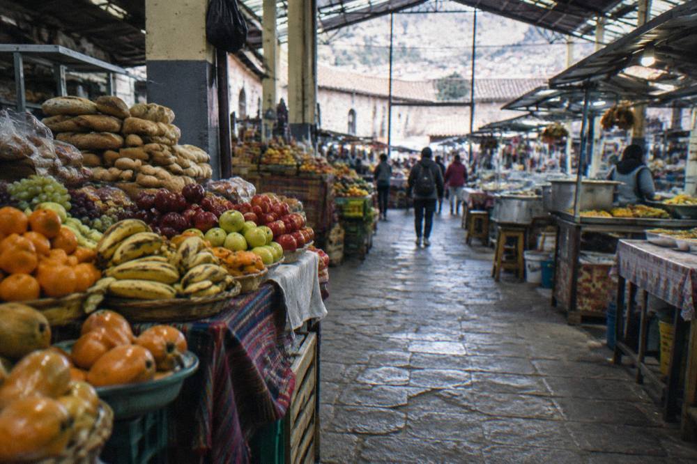 A busy covered market hall with stalls of fruit, bread and cooked food in Cusco