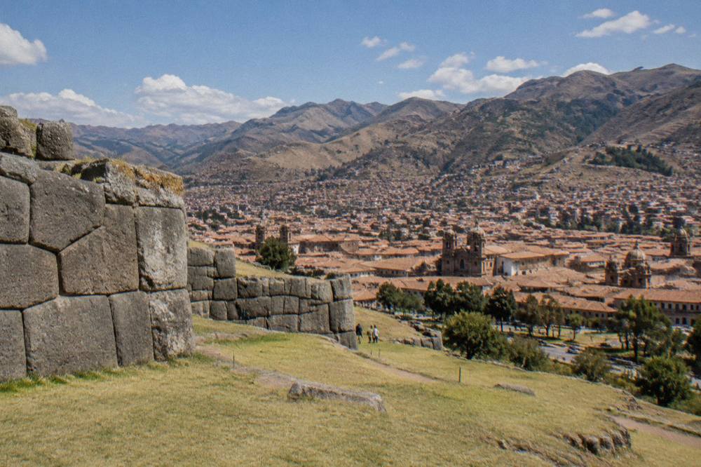 Red tile rooftops and church domes of Cusco seen from a hillside above the city