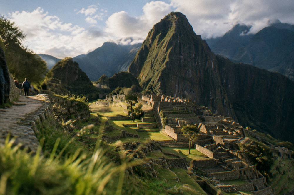 Stone terraces of Machu Picchu with a steep green peak rising behind them under scattered cloud