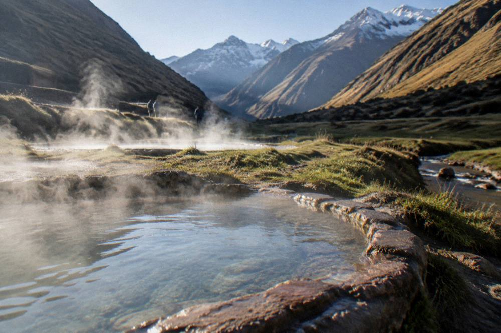 Steaming natural hot spring pools surrounded by grass at the end of a valley