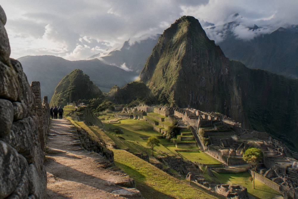 The stone terraces of Machu Picchu with the green peak of Huayna Picchu behind under cloud