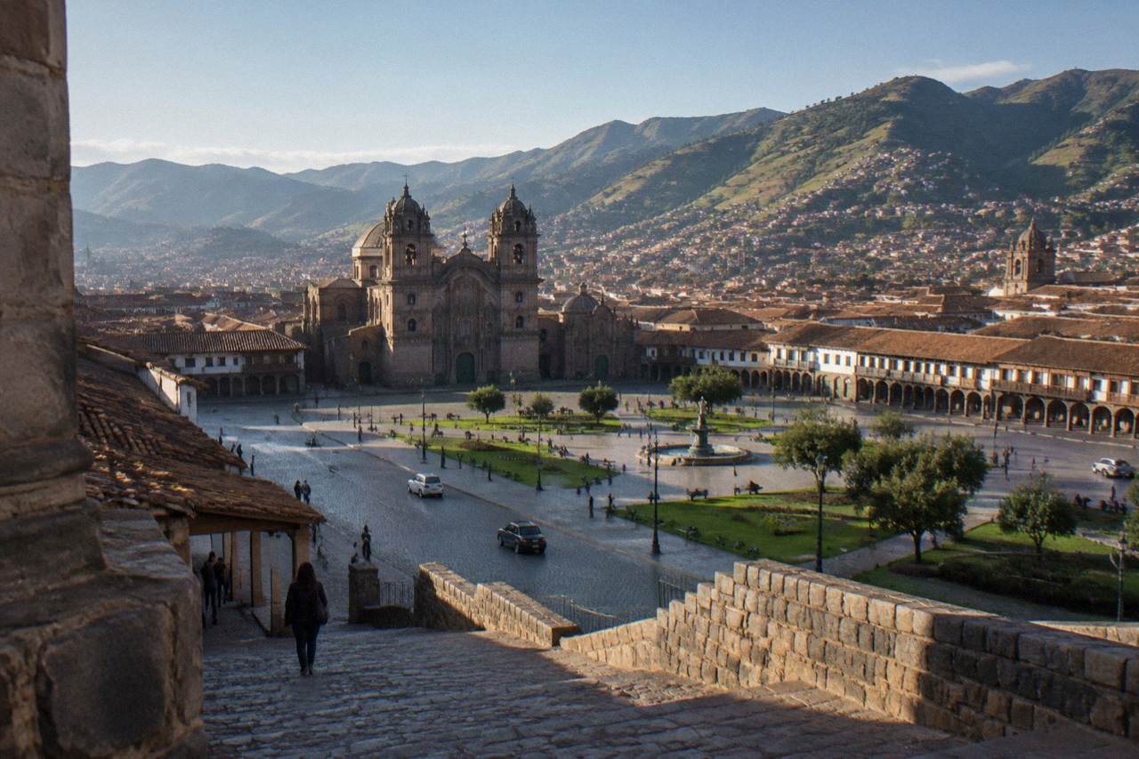 Terracotta roofs of Cusco spreading below green hills under a clear sky