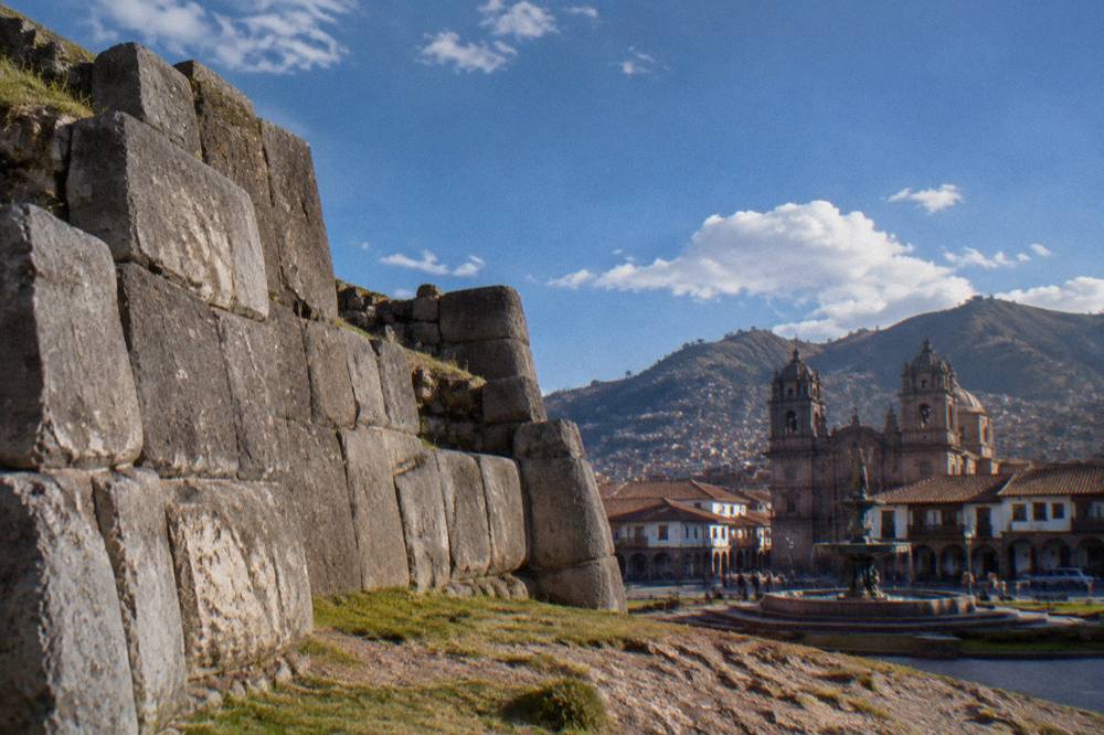 The arcaded colonial buildings and stone fountain of Cusco's main square in late afternoon light