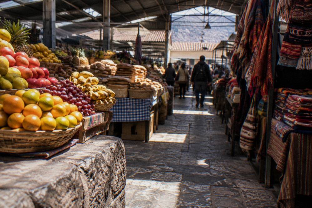 Stalls of fruit, bread and woven textiles under the iron roof of a busy Andean market hall