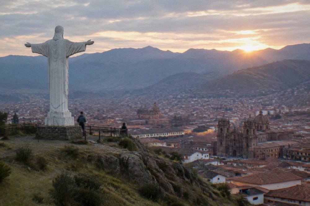 The white statue of Cristo Blanco overlooking the red roofs and church towers of Cusco at sunrise