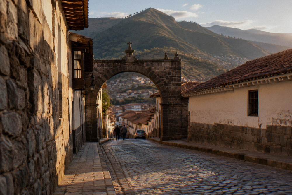 A quiet cobblestone street in Cusco with a stone archway and hills beyond