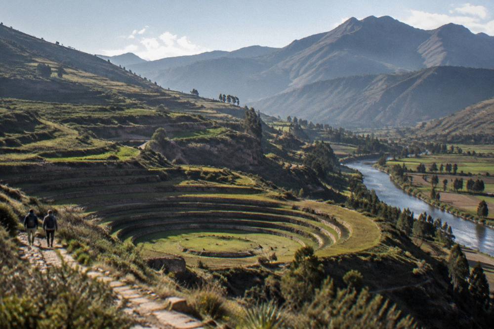 A river running between green valley fields with mountains behind